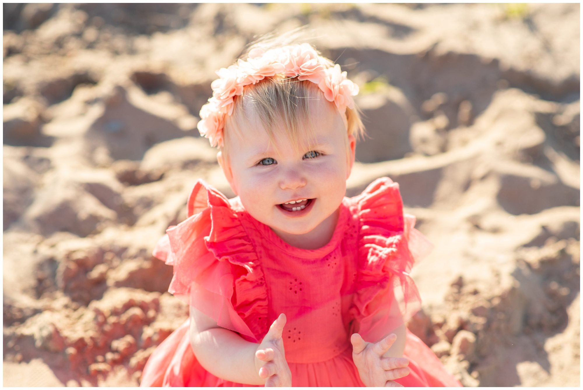 Little girl in bright pink dress sitting in the sand smiling at Port Stanley main beach.