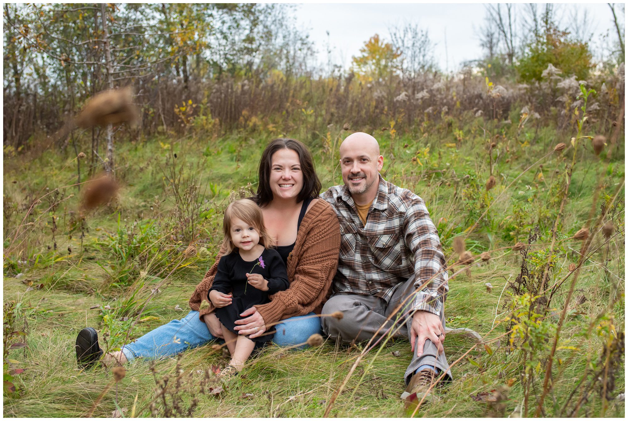 Family of three sitting together in grass at Reforest London.