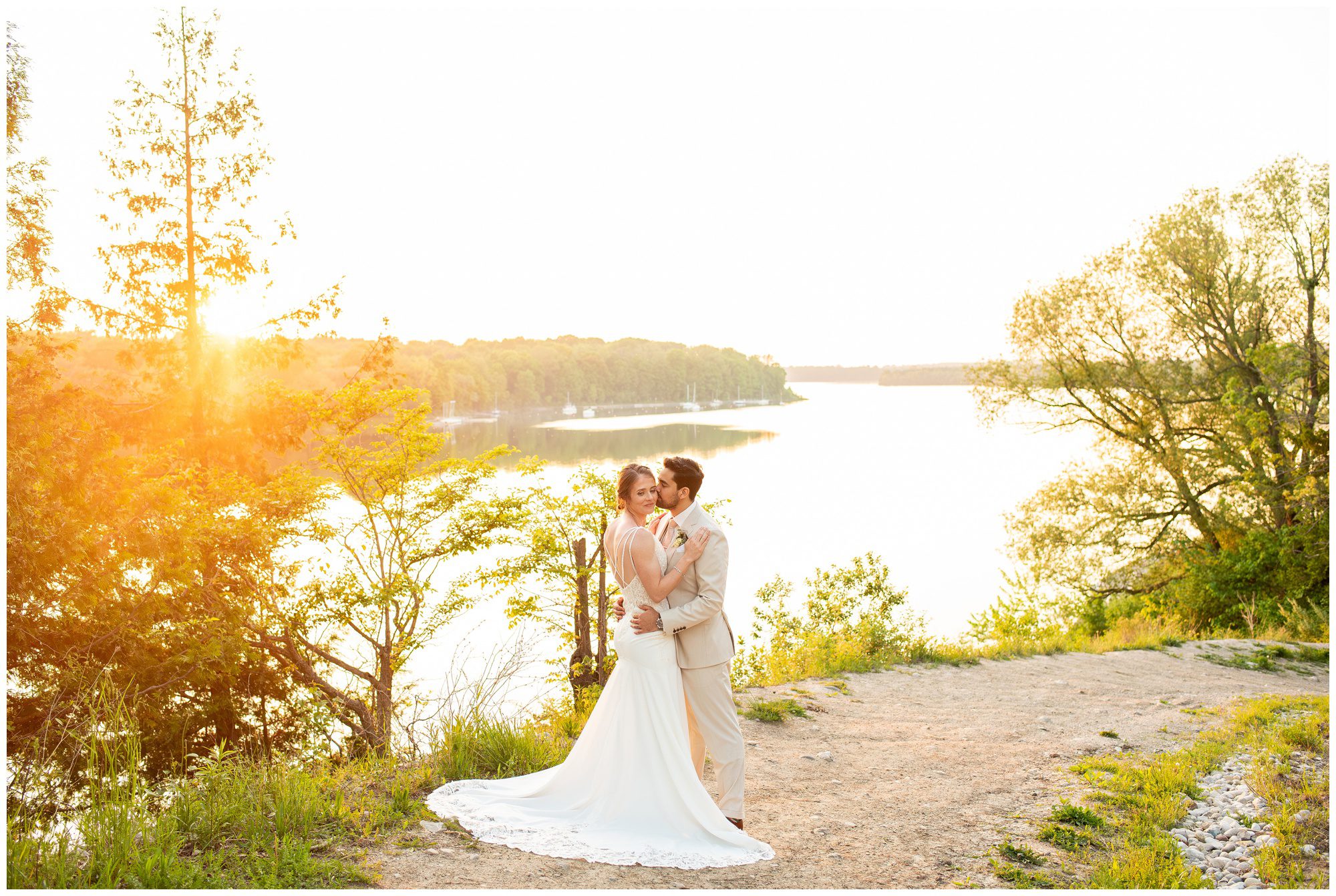 Groom kissing bride on the cheek at golden hour overlooking the river at Forest City National.