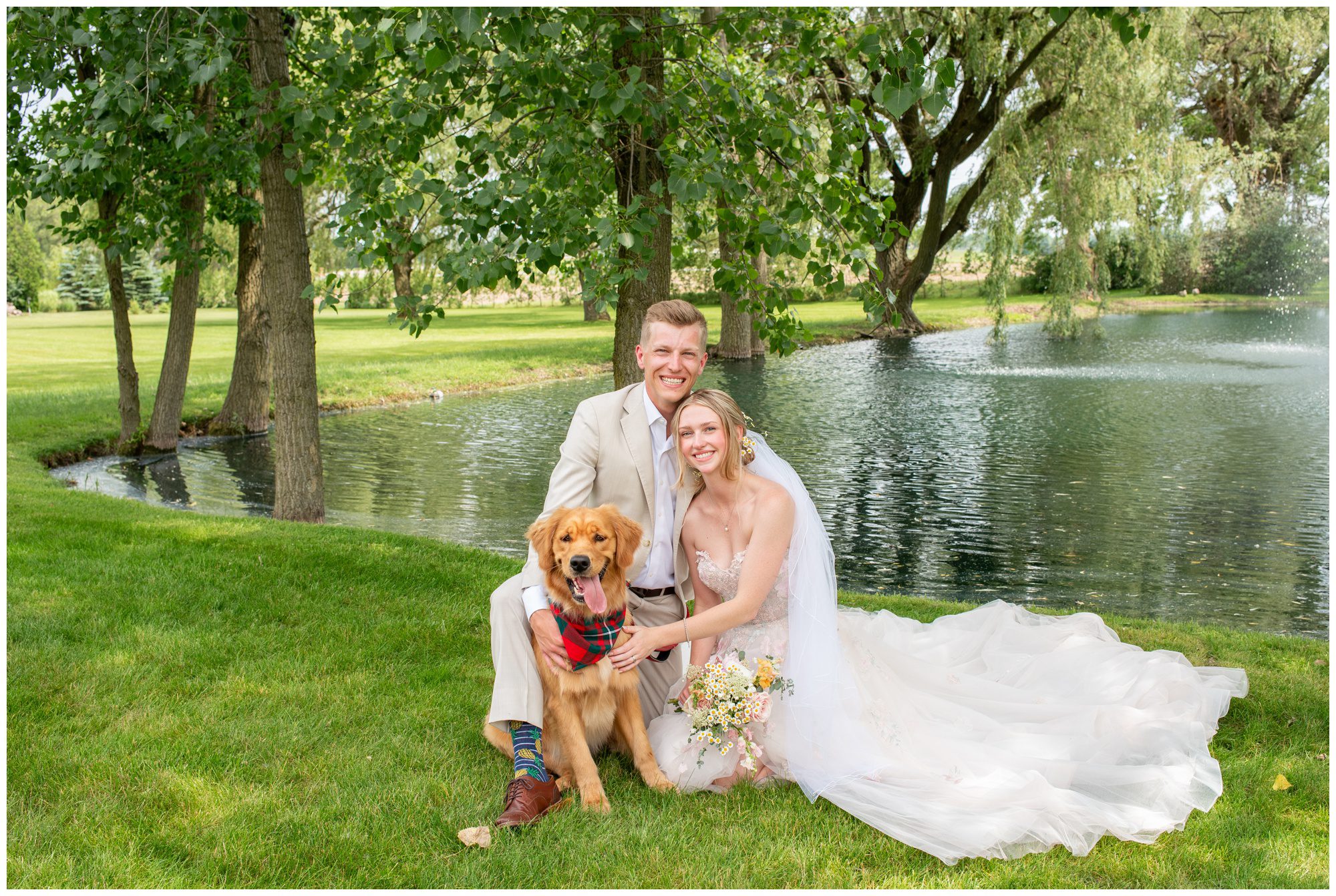 Bride and Groom looking at camera smiling with their golden retriever in front of a pond in London Ontario